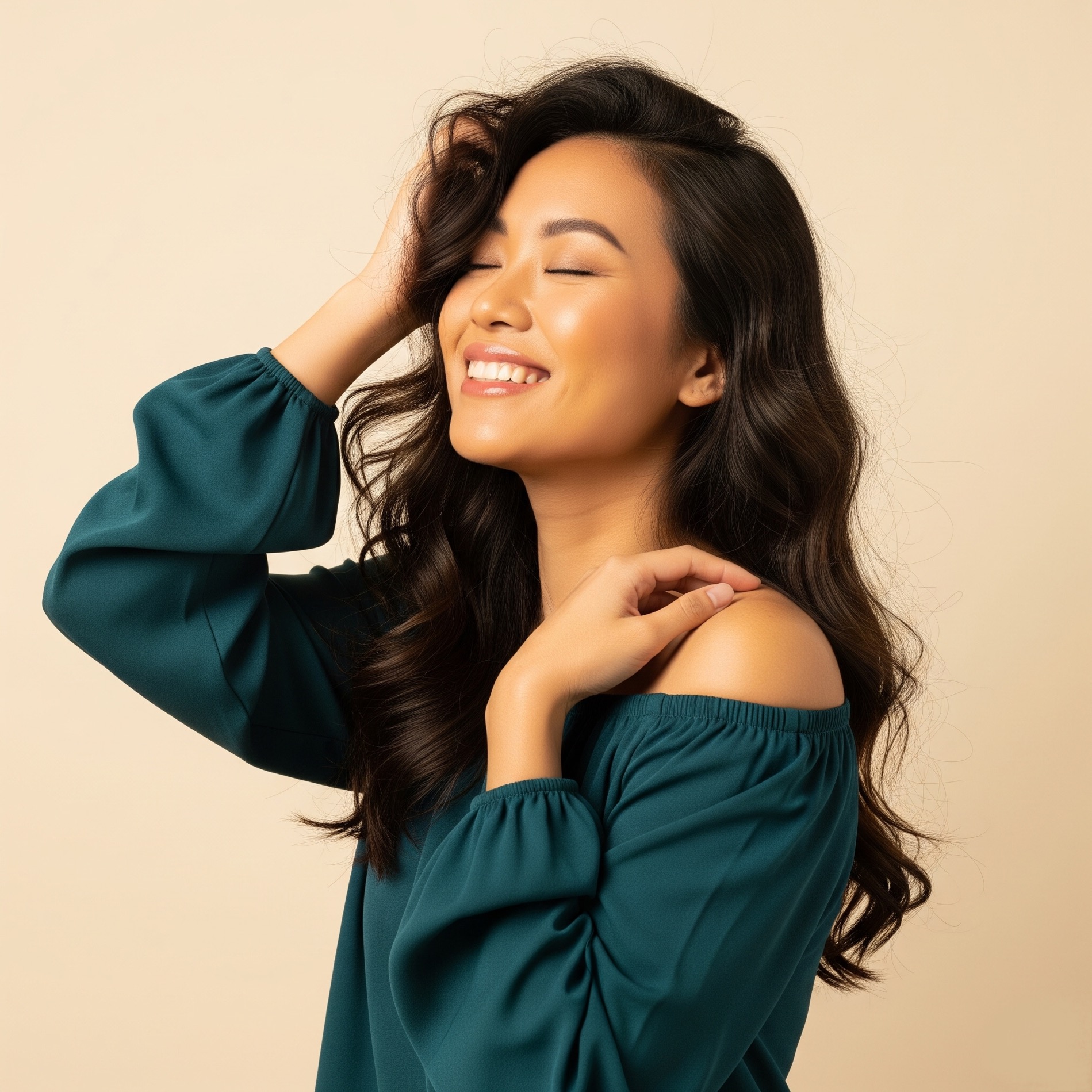 Smiling woman with long, wavy hair wearing a deep teal off-the-shoulder blouse, eyes closed in confidence.